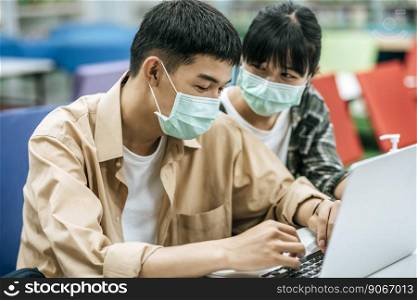 Men and women wear masks and use a laptop to search for books in the library.