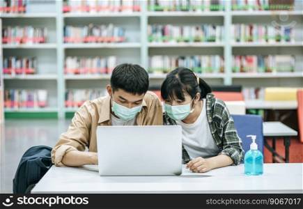Men and women wear masks and use a laptop to search for books in the library.