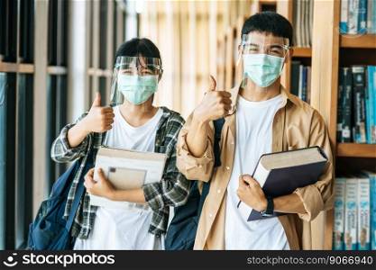 Men and women wear masks to stand, hold books in the library and put their thumbs up.