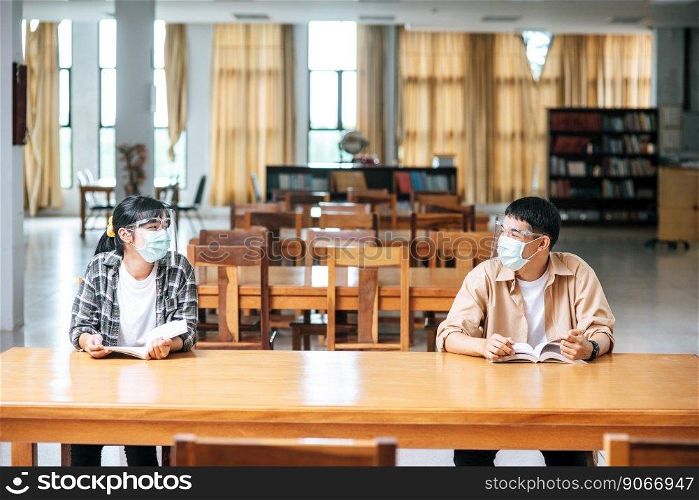Men and women wearing masks sit and read in the library.