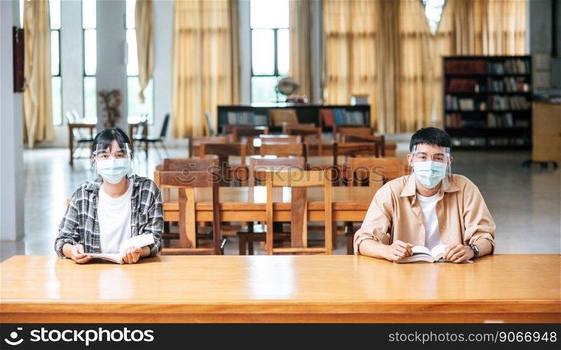 Men and women wearing masks sit and read in the library.