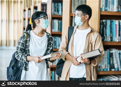 Men and women wearing masks stand and read in the library.