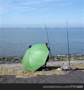 men behind large green umbrella seek protection from the sun white fishing in waddenzee near harlingen in the netherlands on sunny day