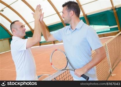 Men doing high five over tennis court net