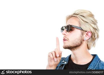 Men fashion, accessories, hairstyle, modeling concept. Artistic hipster blonde man wearing sunglasses showing silence gesture finger on lips profile portrait, studio shot isolated. Hipster artistic man with sunglasses, silence gesture