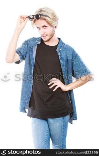 Men fashion, clothing and accessories concept. Artistic hipster guy holding glasses wearing jeans outfit, studio shot isolated.. Artistic hipster guy holding glasses
