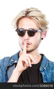 Men fashion, modeling concept. Hipster man wearing jeans outfit and sunglasses making silence gesture studio shot, isolated. Hipster man with sunglasses making silence gesture