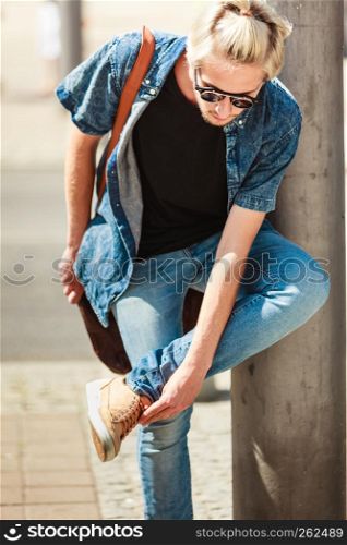 Men fashion, urban style clothing concept. Hipster guy walking through city wearing jeans outfit, male handbag and sunglasses on sunny day. Hipster man walking through city, urban style