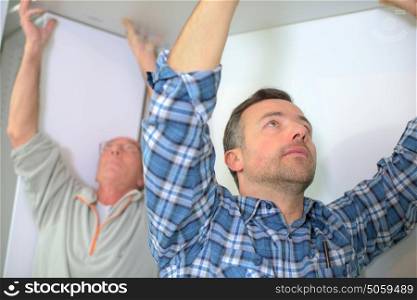 Men fitting plasterboard to ceiling