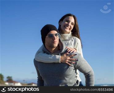 Men Giving Piggy Back Rides At Sunset By The Sea, autumn time. couple having fun at beach during autumn