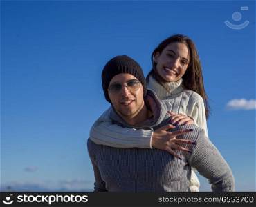 Men Giving Piggy Back Rides At Sunset By The Sea, autumn time. couple having fun at beach during autumn