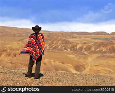 Men in a poncho in the desert. Blue sky and yellow desert.