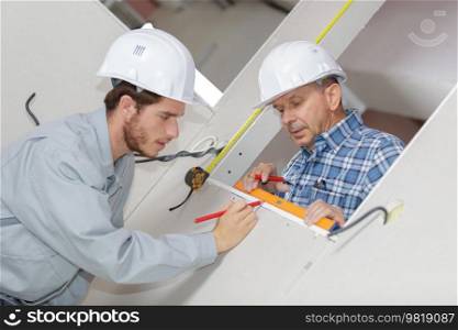 men in uniform and hardhats measuring wall with tape