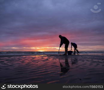 men on normandy beach during colorful sunset look for worms to use as bait for fishing