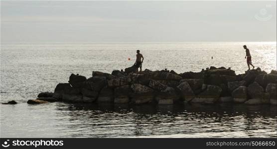 Men on rock groyne by sea, Sant'Angelo, Ischia Island, Campania, Italy