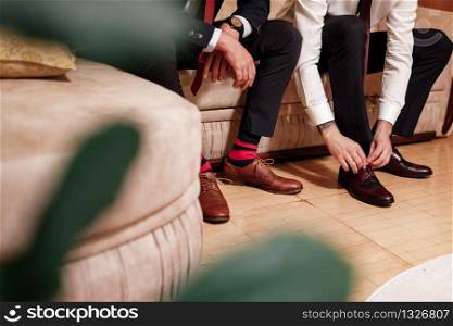 Men&rsquo;s feet in stylish shoes and bright socks. Elegant man dresses shoes. Two men&rsquo;s hands tie shoelaces. Men&rsquo;s fashion. Wedding fashion.