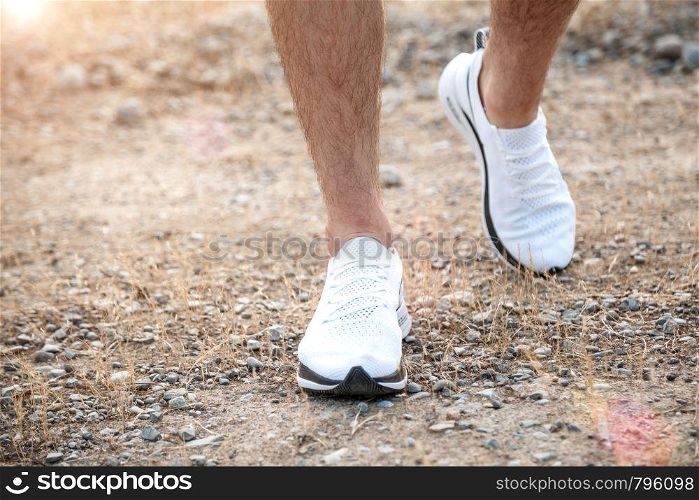 men's feet in white sneakers running over rough terrain. Cross country running with focus on runner's legs.