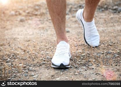 men's feet in white sneakers running over rough terrain. Cross country running with focus on runner's legs.