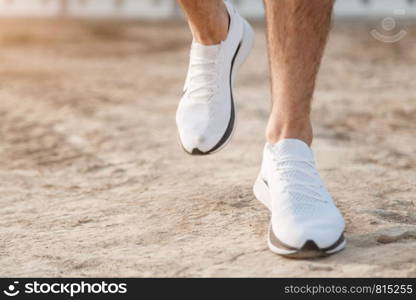 men's feet in white sneakers running over rough terrain. Cross country running with focus on runner's legs.