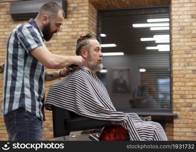 Men&rsquo;s hairstyling and haircutting with hair clipper in a barber shop or hair salon. Shallow depth of field.