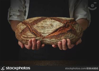 Men&rsquo;s hands hold organic dark bread on a dark background close-up. Men&rsquo;s hands hold organic dark bread