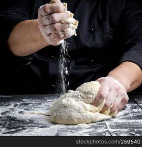 men's hands knead white wheat flour yeast dough on a black wooden table