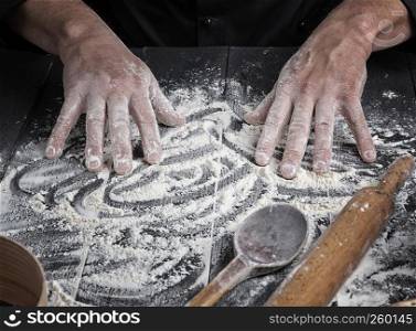 men's hands stir the white wheat flour on a black wooden table