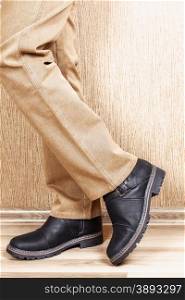 Men&rsquo;s leather shoes and jeans khaki legs. A man stands on a wooden floor near the wall.