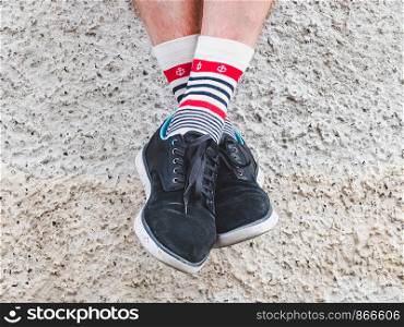 Men's legs in sports shoes and white socks with a bright, sea pattern in the shape of anchors on the background of a rocky shore on a summer, sunny day. Concept of fashion, sport and recreation. Men's legs in sports shoes and white socks