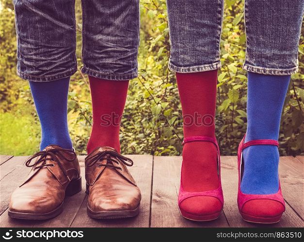 Men's legs in stylish shoes, bright, multi colored, variegated socks with Christmas and New Year's patterns on the wooden terrace on the background of green trees. Beauty, fashion, elegance. Men's legs in stylish shoes, bright, multi colored, variegated socks