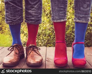 Men's legs in stylish shoes, bright, multi colored, variegated socks with Christmas and New Year's patterns on the wooden terrace on the background of green trees. Beauty, fashion, elegance. Men's legs in stylish shoes, bright, multi colored, variegated socks