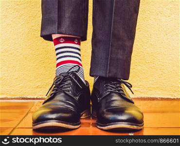 Men's legs, stylish shoes, colorful socks with a pattern in the form of anchors on the background of a yellow wall. Concept of style, fashion and beauty. Men's legs, stylish shoes and colorful socks