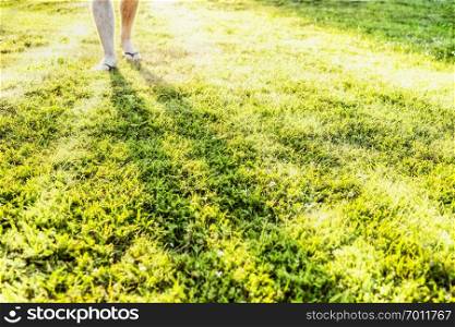 Men’s feet are on the sunlit grassy meadow, Sun rays