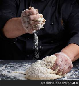 men’s hands knead white wheat flour yeast dough on a black wooden table