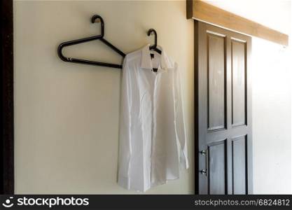Men's white shirt hanging at the wall with sun flare from windows