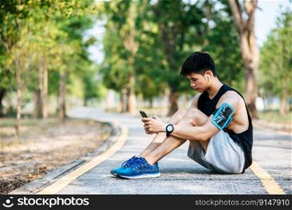 Men sitting and resting after exercising on the roadside and play a smartphone. Selective focus