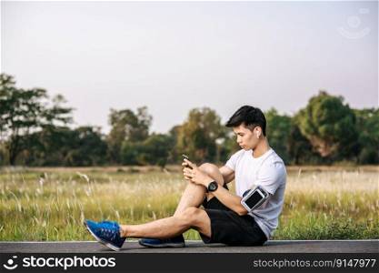 Men sitting and resting after exercising on the roadside and play a smartphone. Selective focus