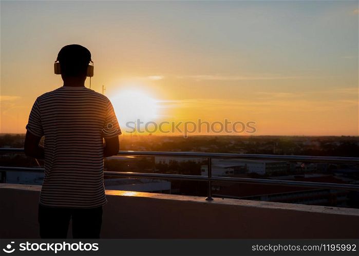 Men standing on headphones at sunset