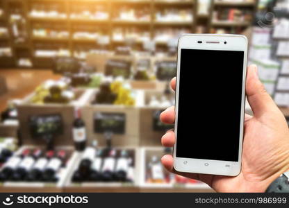 Men use hold smartphone blurred images of Various alcohol bottles in a row at the spirits store background.