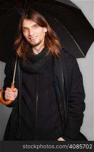 Men winter fashion. Handsome man long hair wearing black coat. Casual look with umbrella. Studio shot on grey