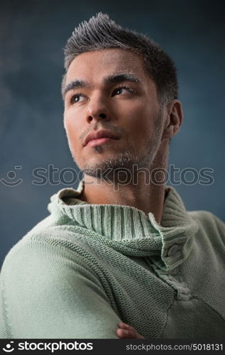 Men winter fashion. Handsome man with black hair wearing green jersey. Covered with snow. Cold. Casual look. Studio shot on smoky dark background.