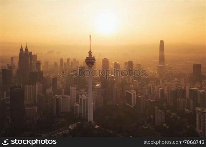 Menara Kuala Lumpur Tower with the sun. Aerial view of Kuala Lumpur Downtown, Malaysia. Financial district and business centers in urban city in Asia. Skyscraper and high-rise buildings at sunset.