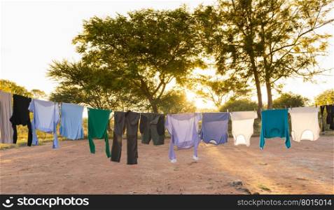 Mens and womens laundry drying on outdoor clothes line with pegs and sun streaming in behind