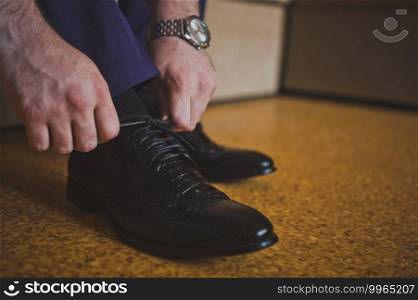 Mens hands tighten the laces of their black shoes.. A man ties the laces of his black shoes 2618.