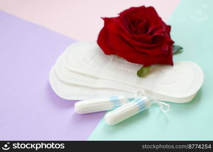 Menstrual pads and t&ons and red rose flower on multicolored background. Aspects of women wellness in monthlies period. Woman critical days gynecological menstruation cycle. Menstrual pads and t&ons with red rose flower on multicolored background