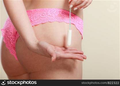 Menstruation time. Hygiene and protection. Close up female in pink panties lingerie holding tampon. Woman presents tampax in her hand.. Girl holding tampon during the monthly cycle