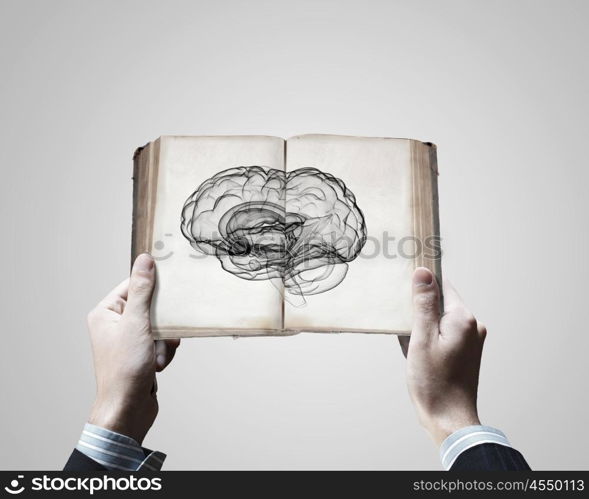 Mental ability. Close up of male hands holding opened book with brain picture