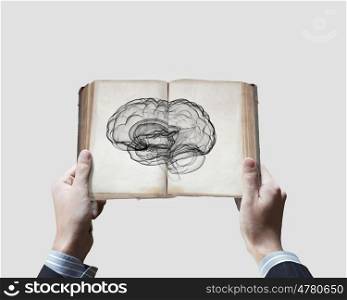 Mental ability. Close up of male hands holding opened book with brain picture