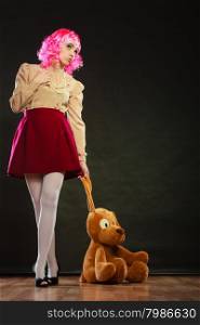 Mental disorder concept. Young childlike woman wearing like puppet doll and big dog toy standing dark black background