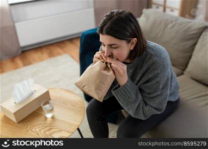 mental health and psychological problem concept - woman having panic attack breathing to bag at home. woman having panic attack breathing to bag at home